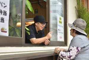  店の窓から住民へ声を掛ける店主の原田さん＝１２日、奄美市名瀬  