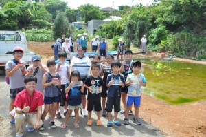 坂口さん（左下）からトウギョの稚魚を受け取った地元の子どもたち＝２７日、知名町瀬利覚