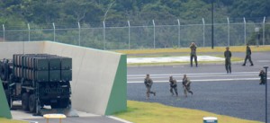 奄美駐屯地のグラウンドで０３式中距離地対空誘導ミサイルの発射装置の方向へ小銃を抱えて走る米兵たち＝１８日、奄美市名瀬