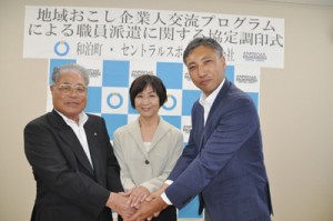 職員派遣の協定を結び、握手を交わす伊地知町長（左）と後藤社長（右）、地域おこし企業人として派遣された久保木さん＝２日、和泊町