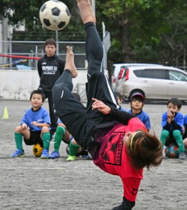 児童たちにオーバーヘッドキックの手本を見せる串山選手＝１１日、奄美市名瀬の朝日小学校校庭