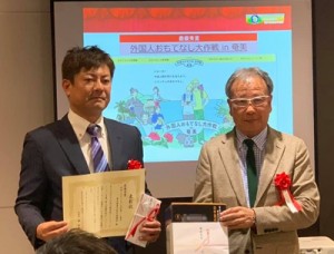 最優秀賞を受け取った奄美産業活性化協議会事務局・奄美市商工情報課情報労政係の中江康仁係長（左）＝同市提供