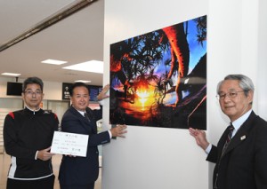 写真を寄贈した（左から）吉行さんと町田酒造の中村社長＝２７日、奄美市笠利町の奄美空港