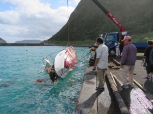 転覆した漁船の引き揚げ作業＝２９日午前９時１０分ごろ、龍郷町安木屋場漁港（町役場提供）