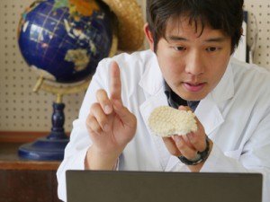 オンライン授業を行うサンゴ研の駒越太郎研究員（手にしているのはアザミサンゴの標本）＝３月、喜界町