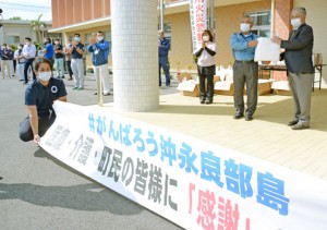 和泊町区長会の代表者に配布用のマスクを手渡す伊地知町長（右）＝１４日、同町役場駐車場