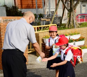 消毒液を持った道添校長に迎えられる児童＝７日、奄美市笠利町の笠利小学校