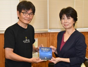 荒木さん（左）から冊子を受け取る奄美図書館の日高館長＝２３日、奄美市名瀬の県立奄美図書館