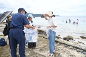 海水浴を楽しむ子どもの保護者らにリーフレットを配る奄美海保職員＝５日、奄美市名瀬の大浜海浜公園