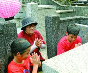 墓前で手を合わせ、先祖の霊を自宅に伴う家族連れ＝３１日、奄美市名瀬の永田墓地