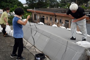 トタンが飛ばないよう、屋根の上で作業する住民ら＝４日、奄美市笠利町
