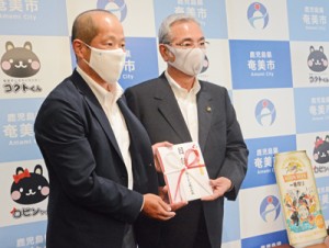 寄付金を朝山市長に手渡すキリンビール鹿児島支店の横松支店長（左）＝２９日、奄美市役所