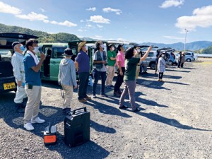 秋空を舞うサシバを見上げる観察会の参加者と解説をする与名正三さん（左手前）＝１１日、宇検村宇検集落漁港