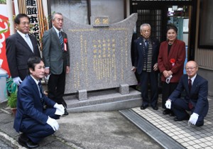 ゆずり葉の郷の発展に貢献した故人が刻名された記念碑と喜入理事長（左奥）、三浦所長（同手前）ら＝１５日、奄美市名瀬の同施設道場前