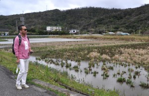 スマホから流れる観光案内を聞きながら秋名集落の田んぼ道を歩く勝さん＝１日、龍郷町