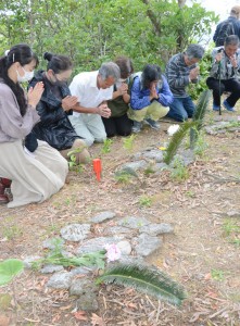 ソテツの葉などをささげ、手を合わせる参列者＝２５日、奄美市笠利町