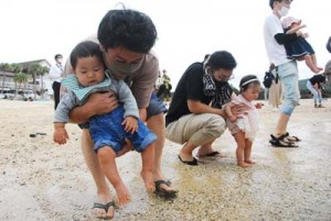 無病息災を祈って赤ちゃんの足を海水に浸す家族ら＝１４日、奄美市笠利町の用安海岸   