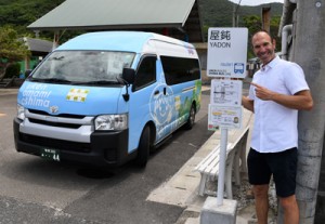 宇検村を運行するラッピングバスと停留所の新しい標識をデザインしたマットさん＝４日、同村屋鈍 