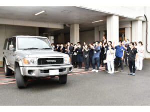 同僚らに見送られ病院を後にするＤＭＡＴメンバーを乗せた車両＝２２日、奄美市
