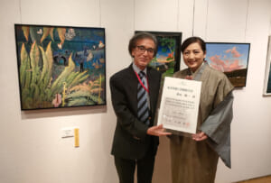 大賞を受賞した横山陽一さん（左）。左の絵が大賞作品「けんむんの社」＝２６日、奄美市笠利町